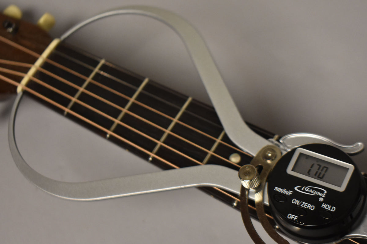 A digital caliper measures the guitar's nut width at 1.70 inches, showing the dark fretboard, light frets, and strings.