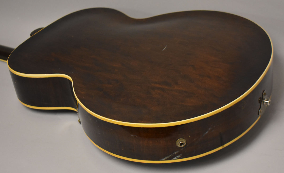 The guitar's dark sunburst back and side are visible, with cream binding, a jack input, and a strap button.