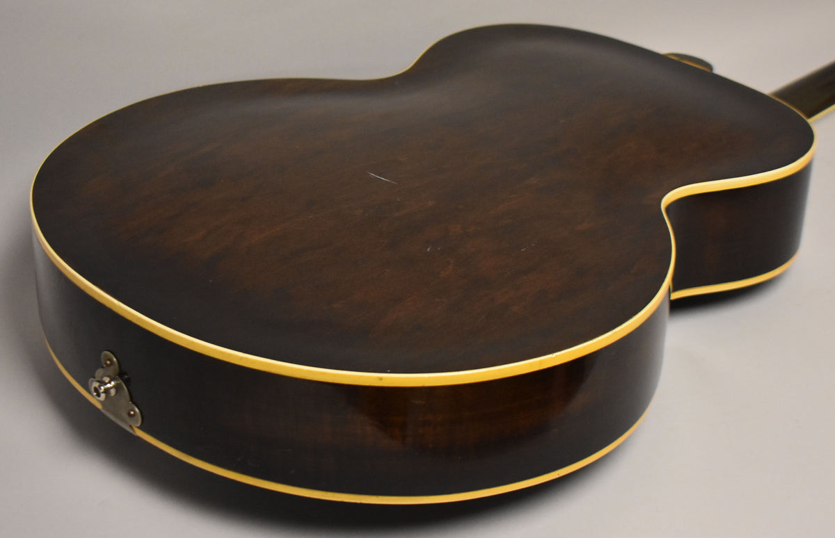 The dark sunburst hollowbody guitar's back and side are visible, showing binding, a jack plate, and light scratches on the finish.