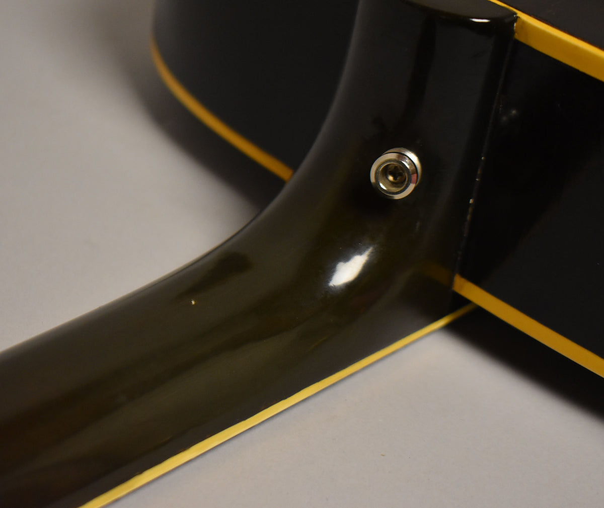 Close-up of the guitar's dark neck heel, showing the input jack and yellow binding, with minor finish wear visible.