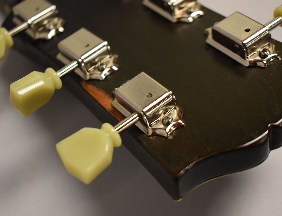 Close-up of the dark brown headstock with three cream-colored tuning pegs and chrome tuners, showing some finish wear on the edge.