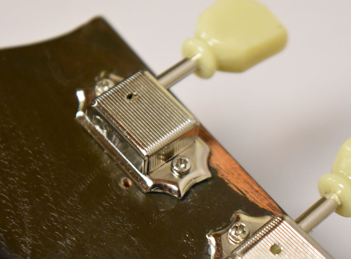 Close-up of the headstock's rear, showing two chrome tuners with ribbed casings and cream plastic buttons, mounted on a dark, worn finish.
