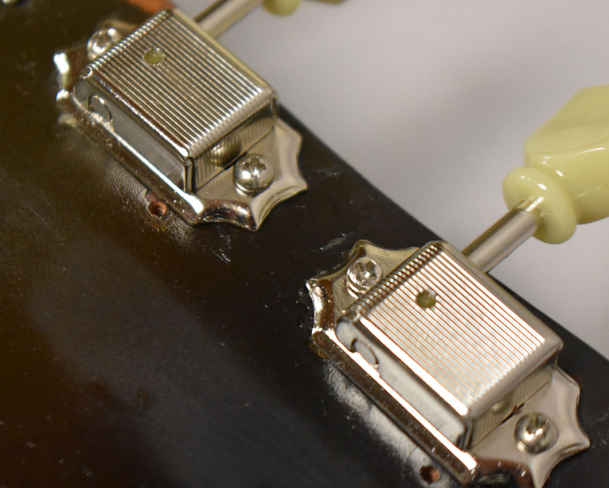 Close-up of two chrome-plated, ribbed tuners with cream buttons on a dark brown headstock, showing minor wear and screw holes.