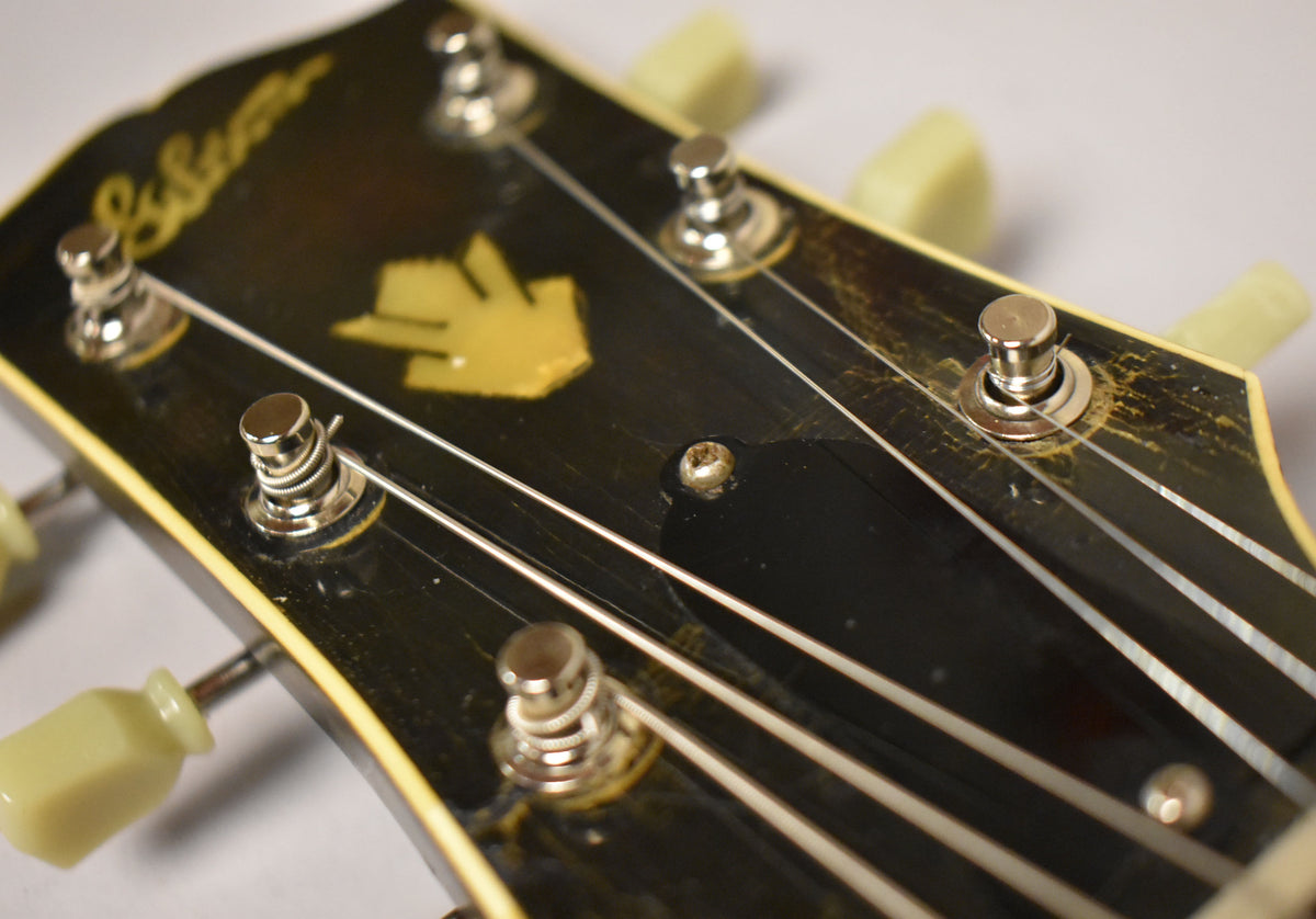 Close-up of the black headstock with a yellow inlay, showing six chrome tuners with cream buttons and heavy finish checking.