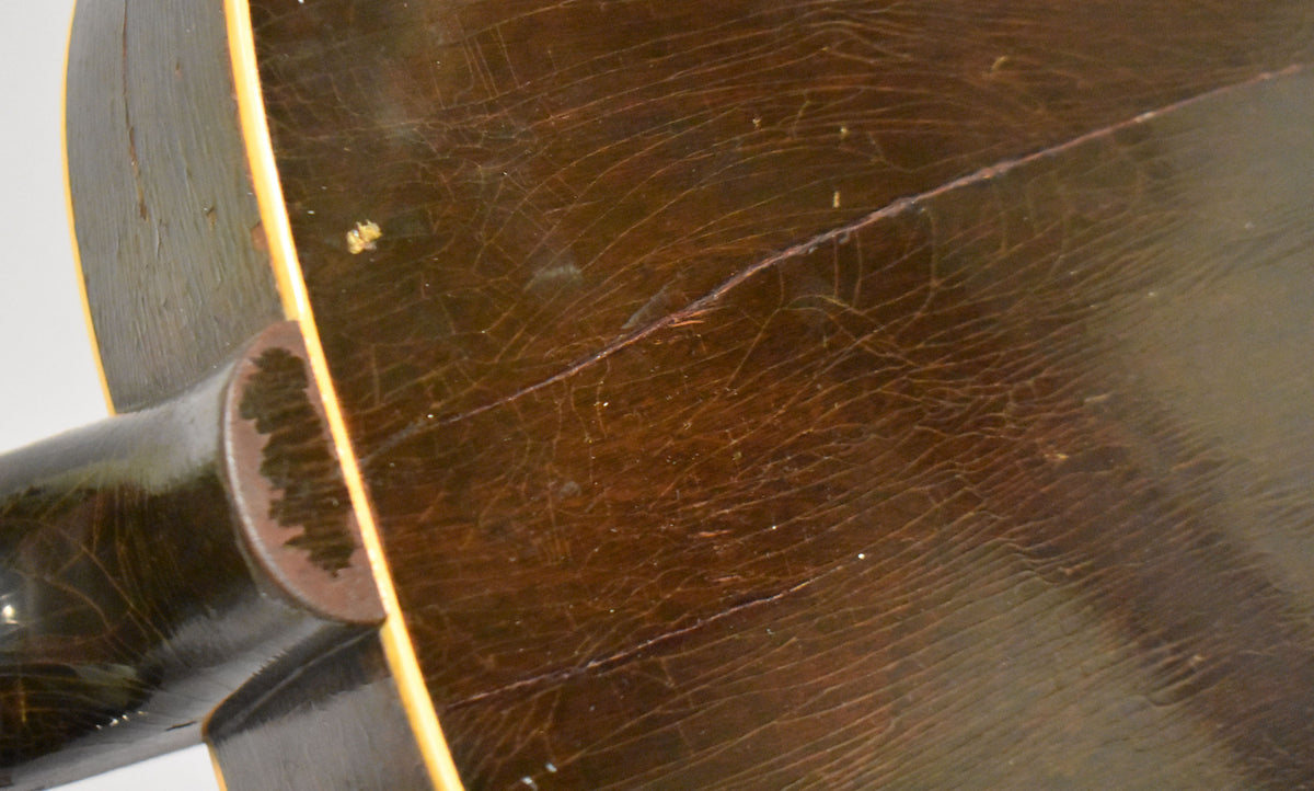 Close-up of the guitar's dark brown back, showing extensive finish checking, a long crack, and a worn heel cap.