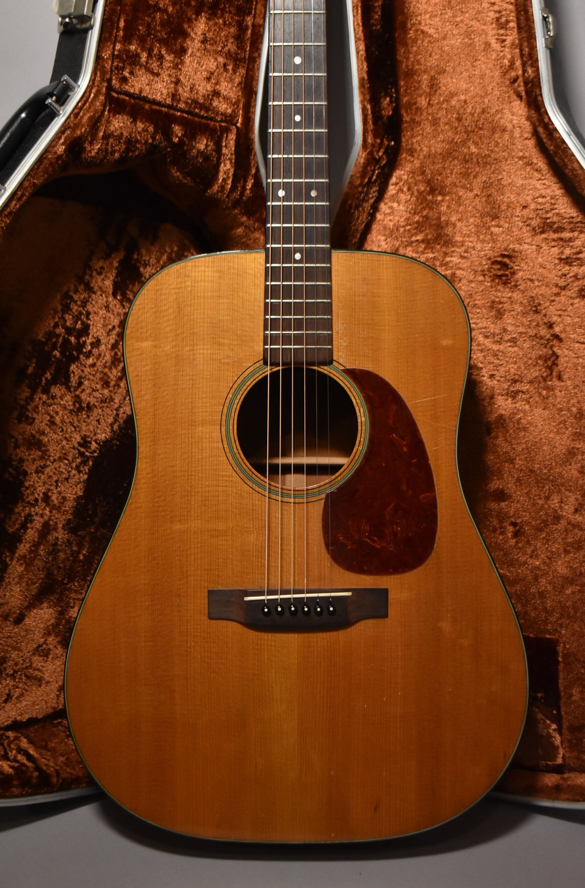 Full front view of a natural finish acoustic guitar with a dark tortoise pickguard, showing wear and checking on the body.