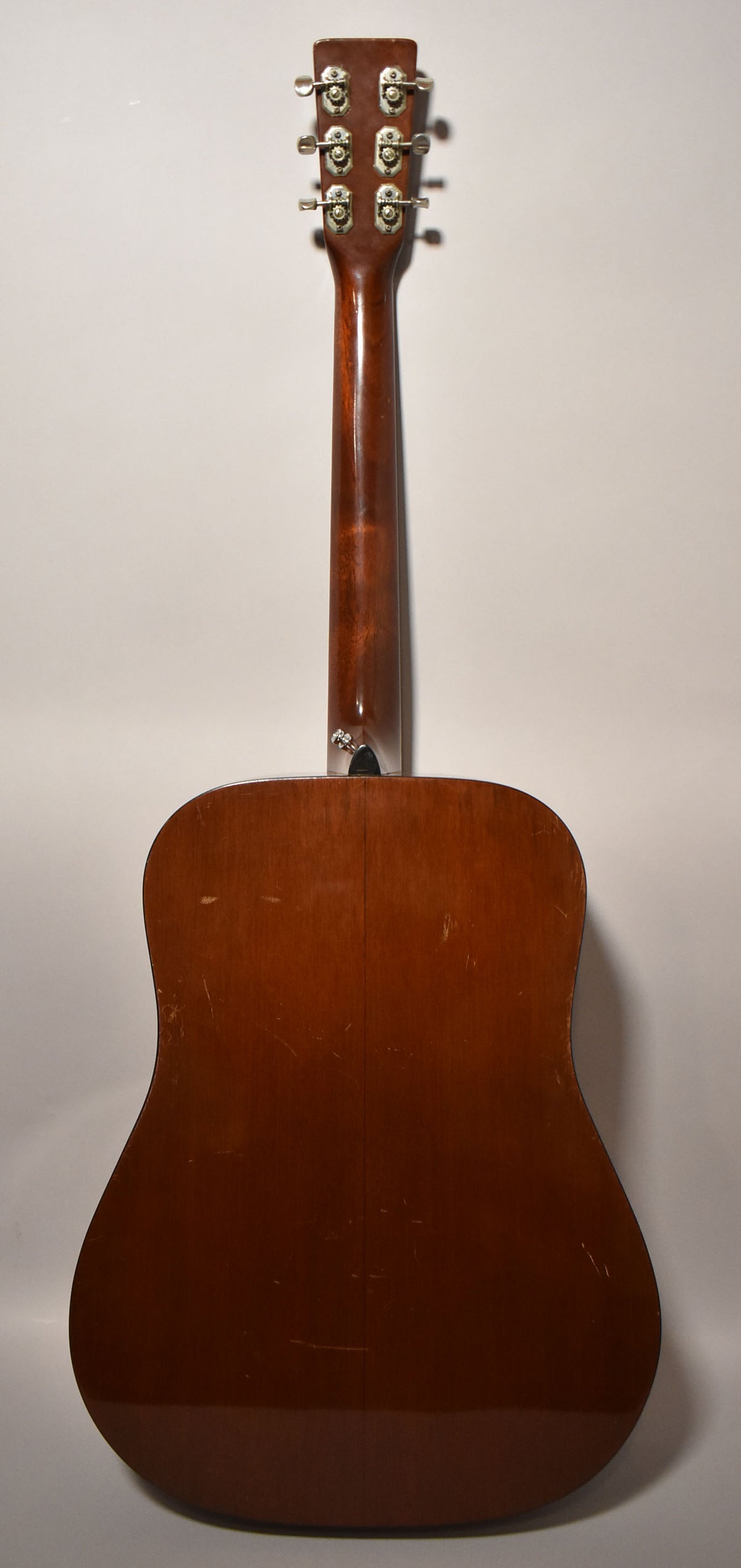 The back of a natural finish dreadnought acoustic guitar, showing the headstock, neck, and body with visible scratches and wear.