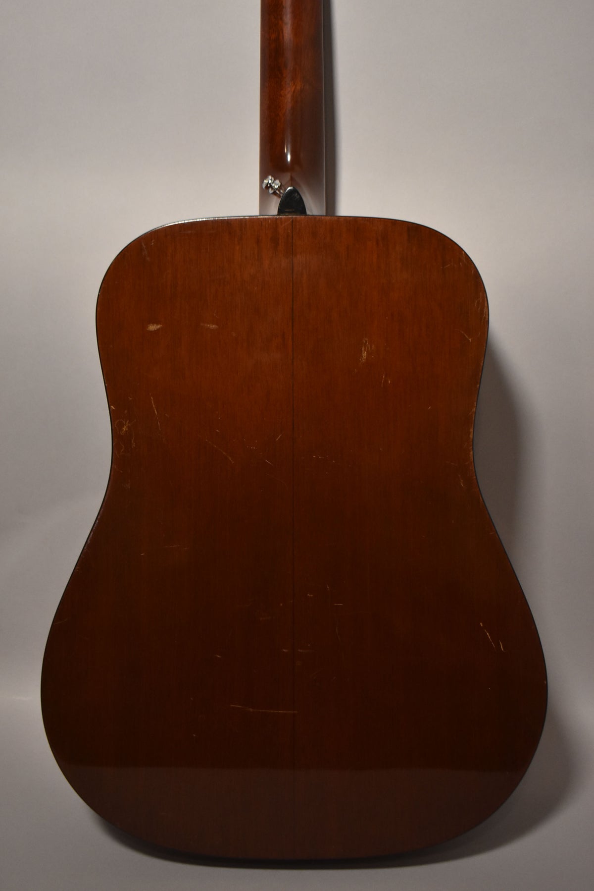 The guitar's dark brown back and neck are shown from behind, with many scratches and scuffs visible on the body.