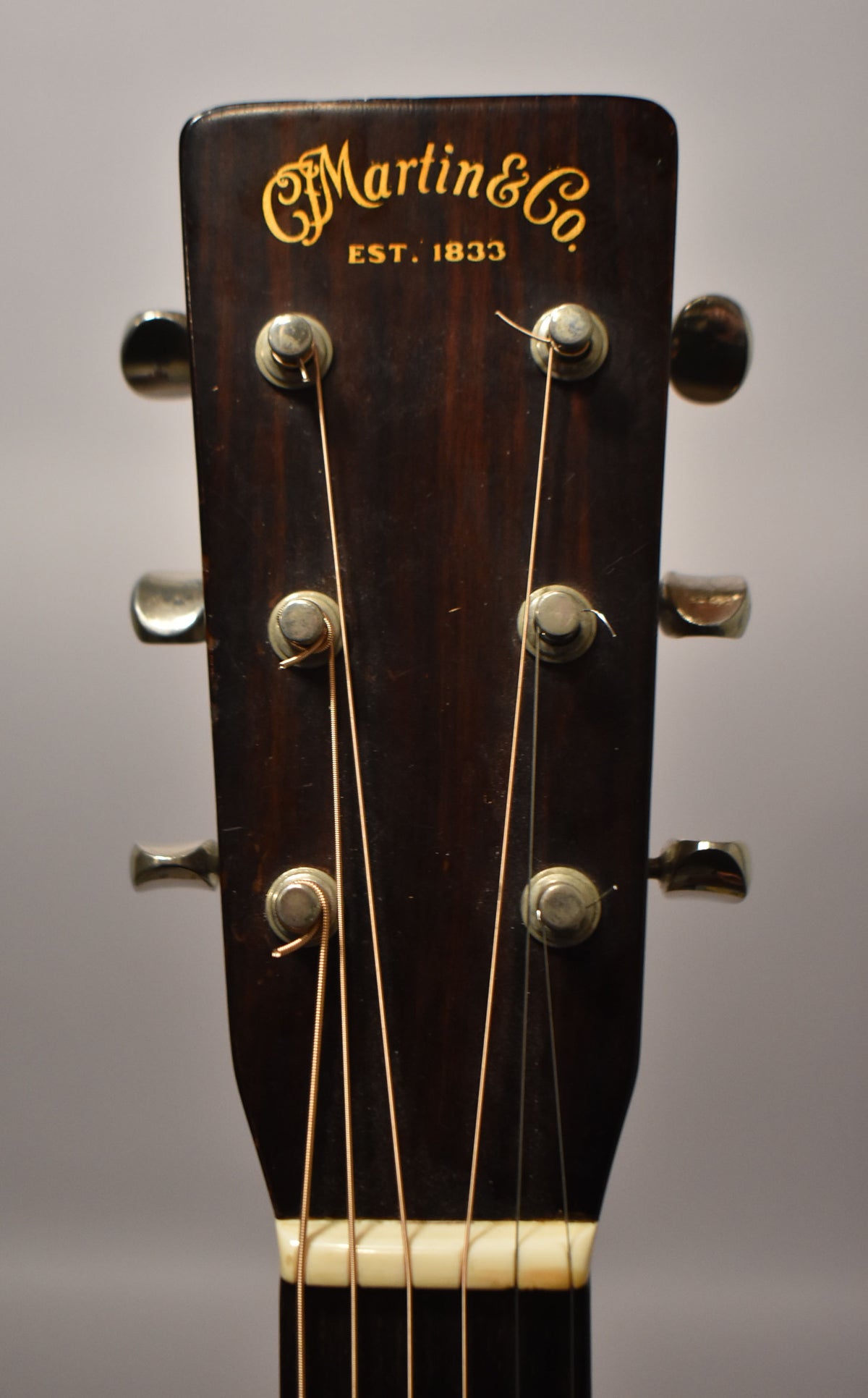Close-up of the dark brown headstock, showing six chrome tuners, a cream nut, and light strings, with some finish wear.