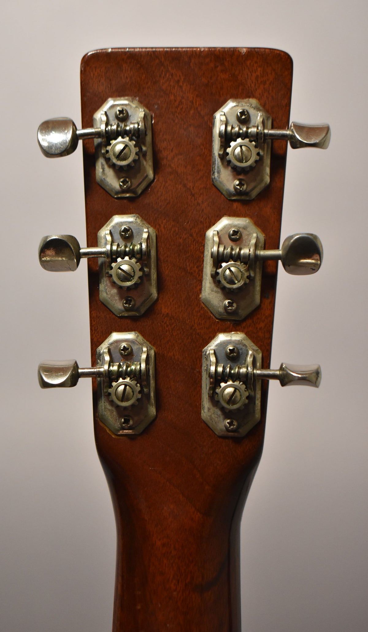 Rear view of the guitar's headstock and neck, showing six tarnished open-gear tuners with metal buttons on a dark wood finish.