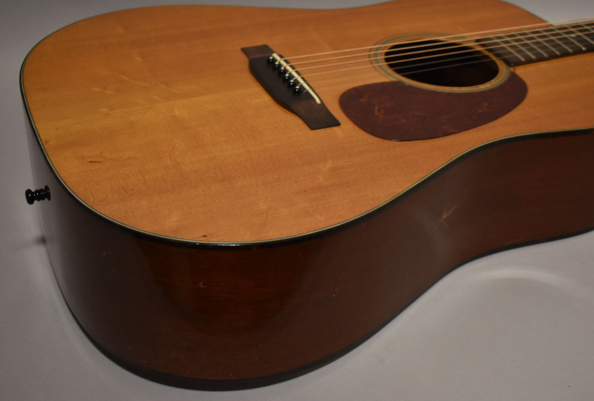 The guitar's natural finish top and dark sides are visible from the lower bout, showing a black endpin and some surface wear.