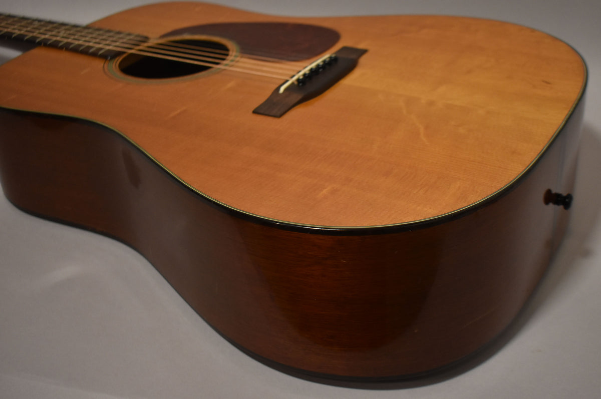 Angled view of the natural-finish dreadnought acoustic guitar body, showing the soundhole, pickguard, bridge, and dark sides with minor wear.