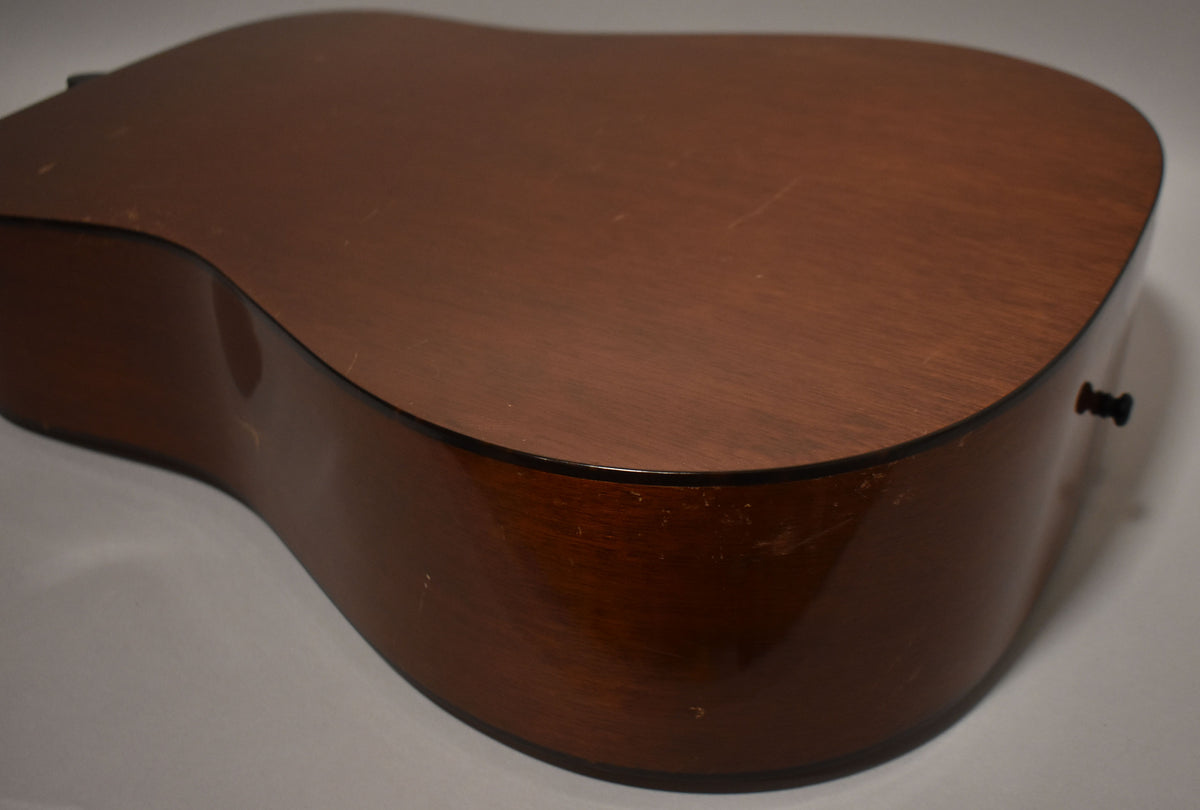 The lower bout of a natural finish acoustic guitar, showing the worn, scratched back and glossy side with a black end pin.