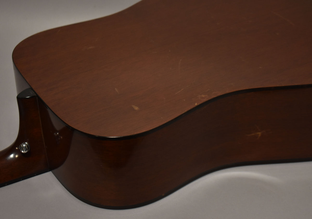 The lower bout and neck heel of a natural finish acoustic guitar, showing wear and scratches on the top and side.