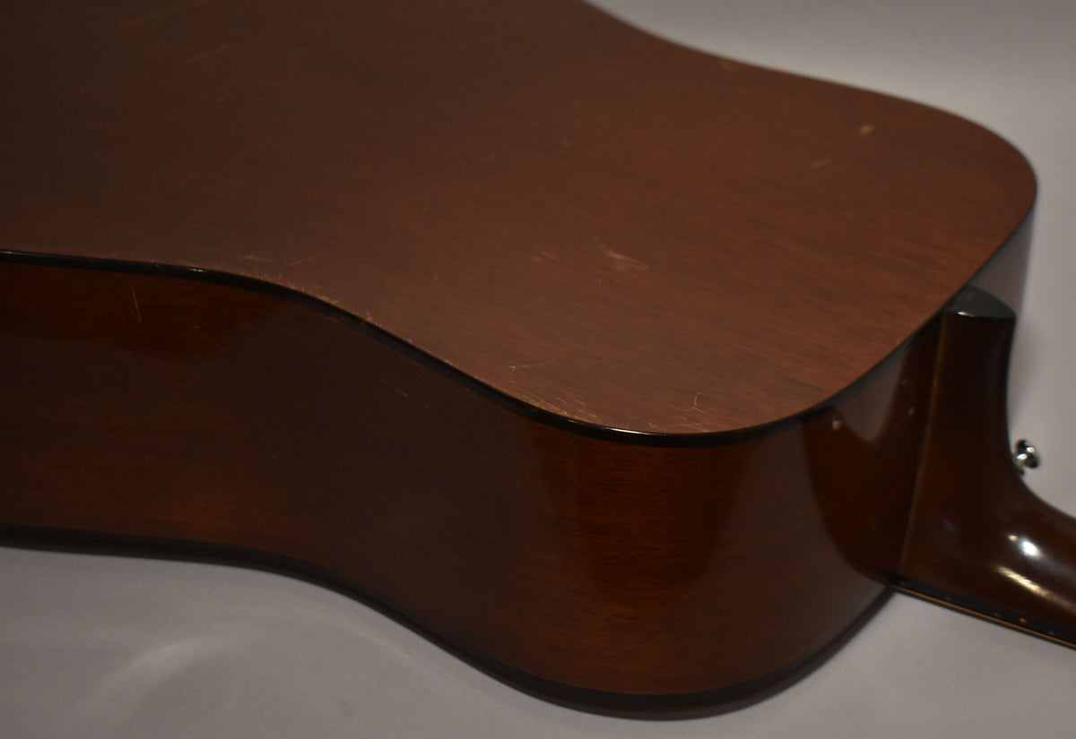 The lower bout and side of the natural finish dreadnought show light wear and scratches, with the heel of the neck visible to the right.