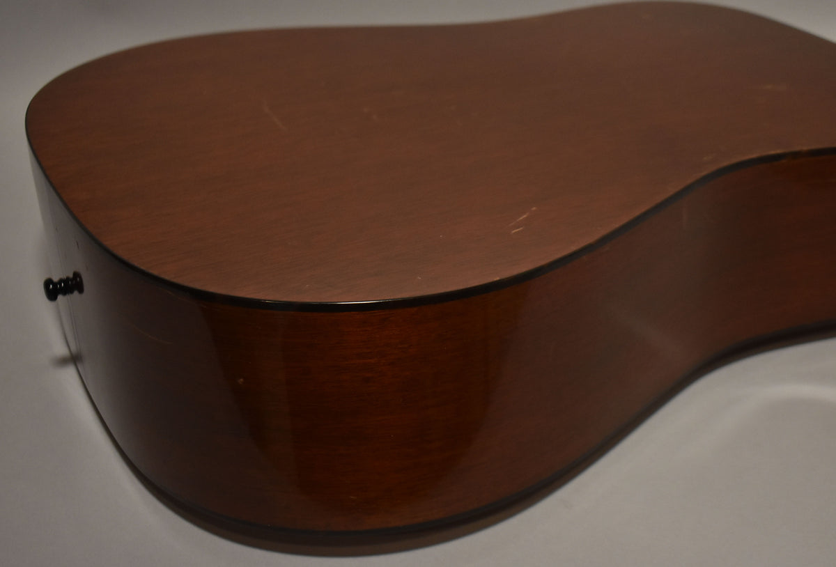 The guitar's lower bout and side, showing a natural finish with light scratches and a black end pin.