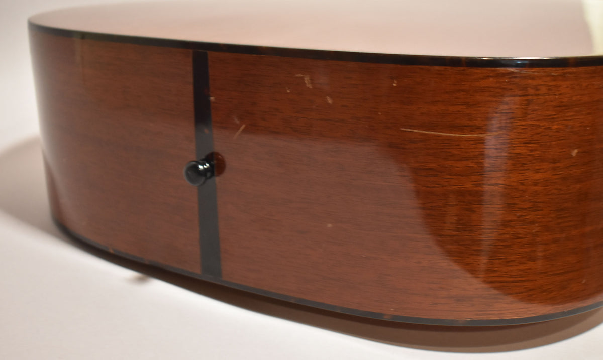 The lower bout of the guitar's natural finish mahogany body, showing a black endpin, dark binding, and light surface scratches.