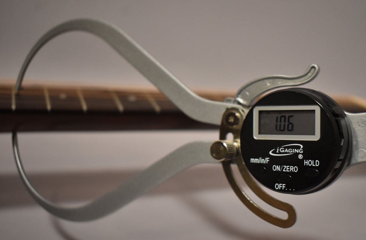A digital caliper measures the neck thickness at the 5th fret, displaying "1.06" on its screen.