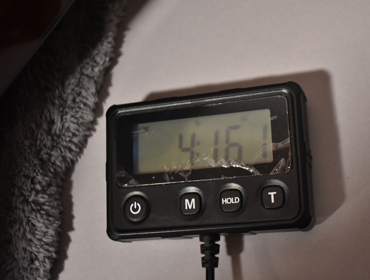 A close-up of a digital scale displaying "4 lb 16 oz" with a cracked screen, next to a gray plush guitar case lining.