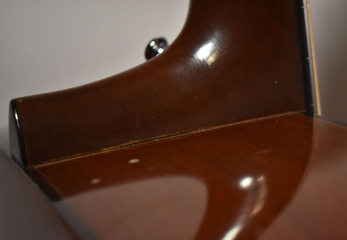 Close-up of the guitar's dark brown neck heel, showing some finish wear and a thin crack along the joint with the body.