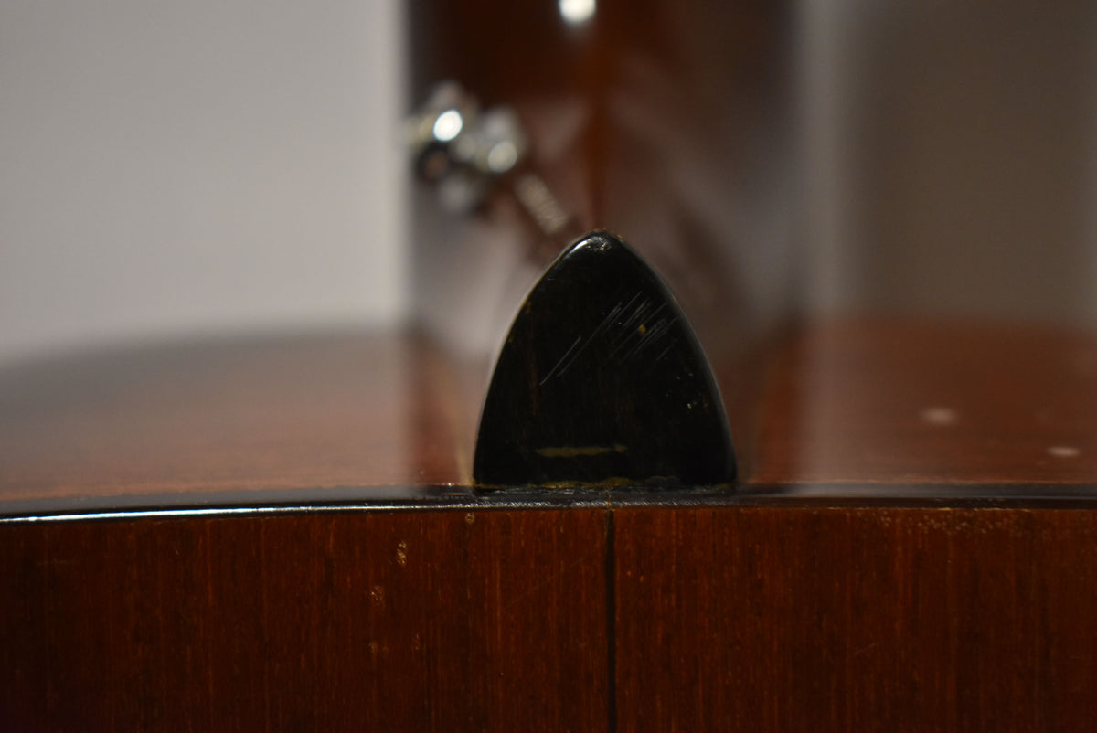 Close-up of the guitar's dark brown heel cap, showing visible scratches and wear on its glossy surface and surrounding wood.