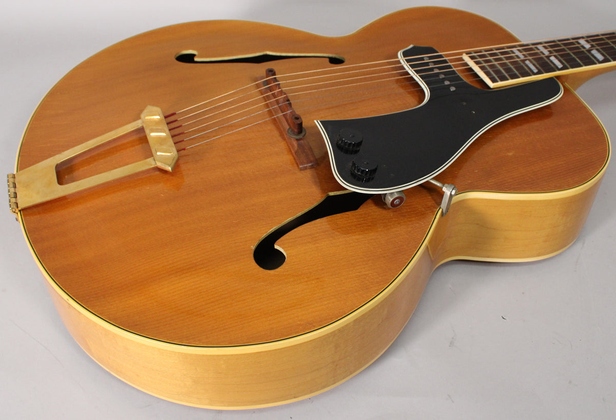 Upper body of a natural finish archtop guitar, showing a black pickguard with two black control knobs and a DeArmond pickup.