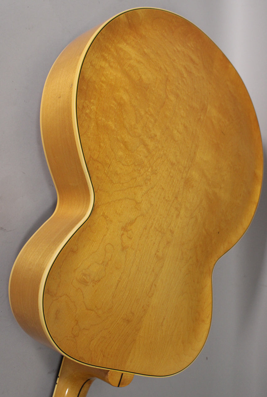 The guitar's light natural finish back and side are visible, with visible wood grain and some light finish checking.