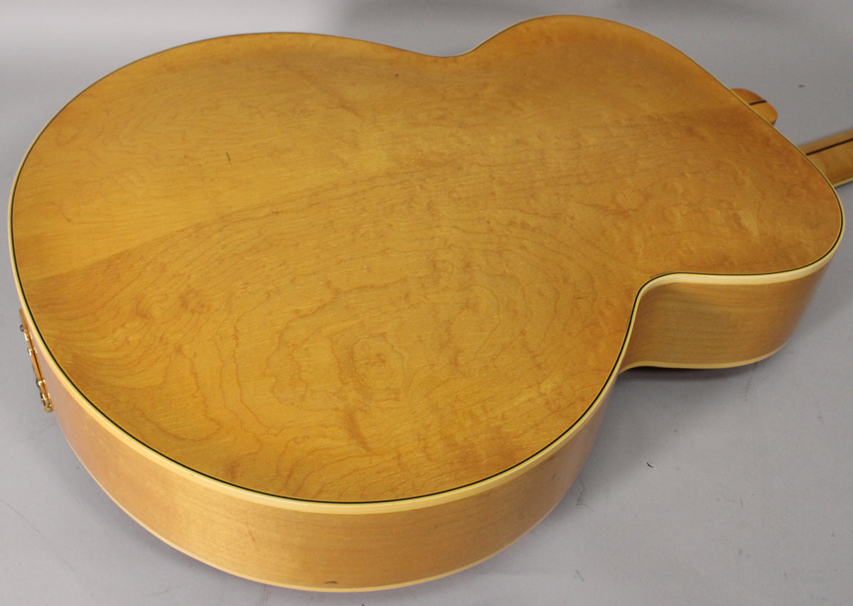 The guitar's light natural finish back and sides are shown from the lower bout, with some light wear and wood grain visible.