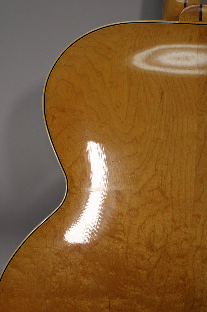 Close-up of the guitar's lower bout, showing the natural finish with prominent wood grain, light checking, and a few small dings.