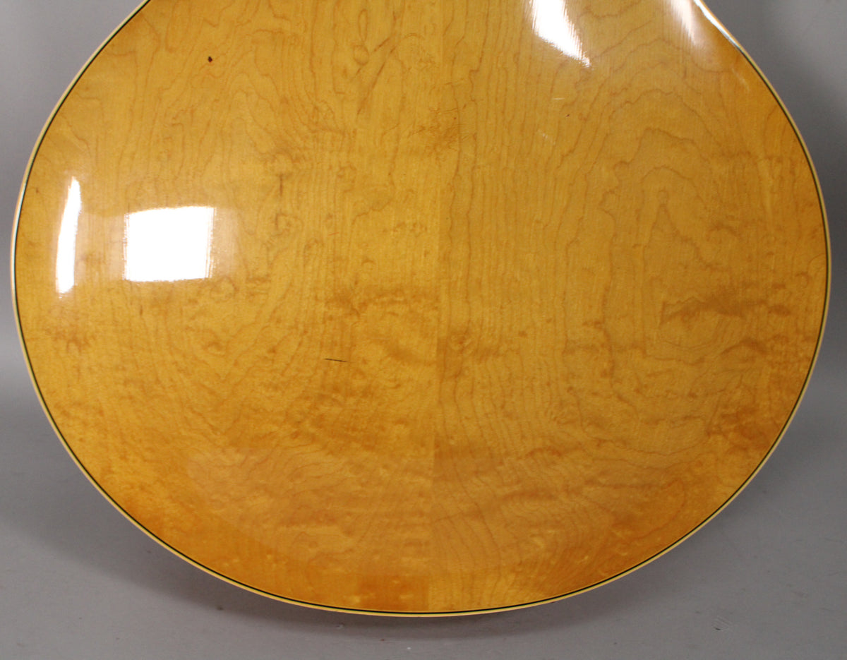 The guitar's light natural finish back shows subtle wood grain, with some light scratches and a small dark mark near the top.