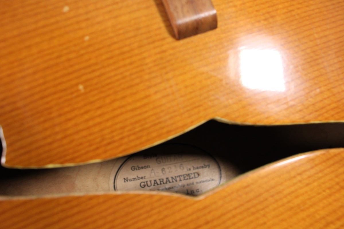 Close-up of the guitar's f-hole, revealing the internal label with "Gibson Number A-6236 GUARANTEED" and a glossy natural finish.