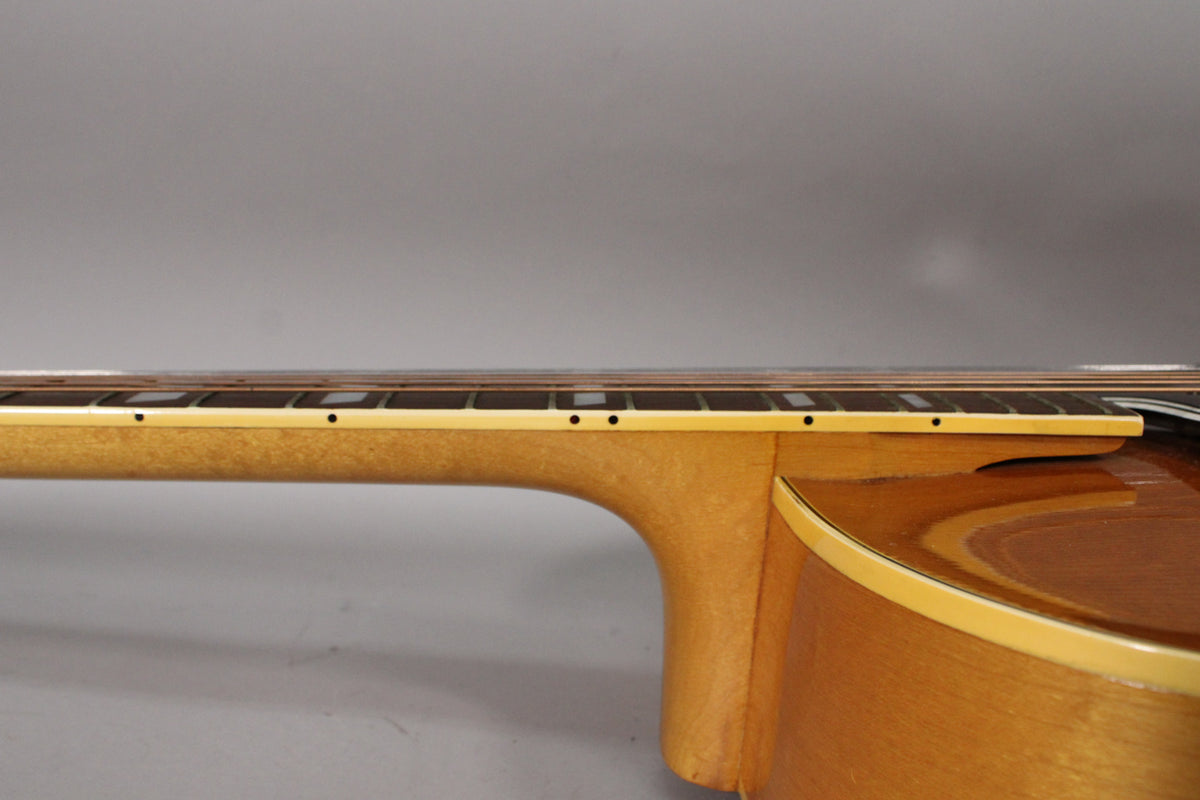 The natural finish archtop guitar's neck and upper body are visible from the side, showing the fretboard with block inlays and side dots.