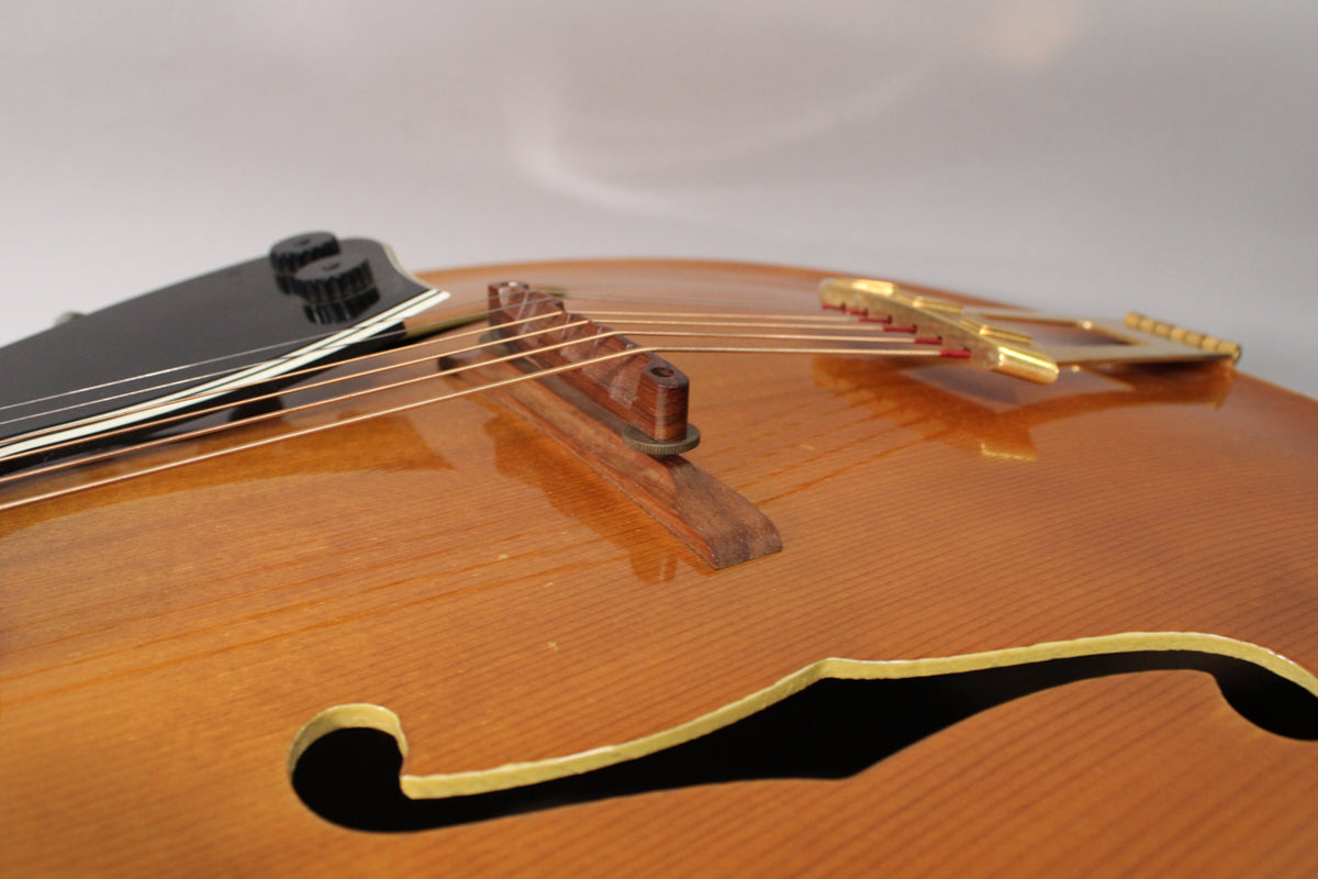 Close-up of the guitar's glossy natural finish body, showing the f-hole, wooden bridge, gold tailpiece, and black floating pickup.