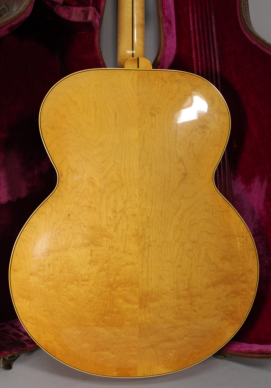 The guitar's full back is visible, showing a natural finish with prominent flame maple grain and light checking.