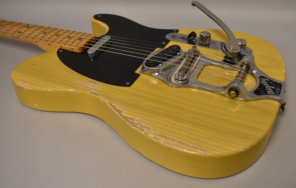 Upper body of a butterscotch blonde electric guitar with a black pickguard, Bigsby vibrato, and heavy finish wear.