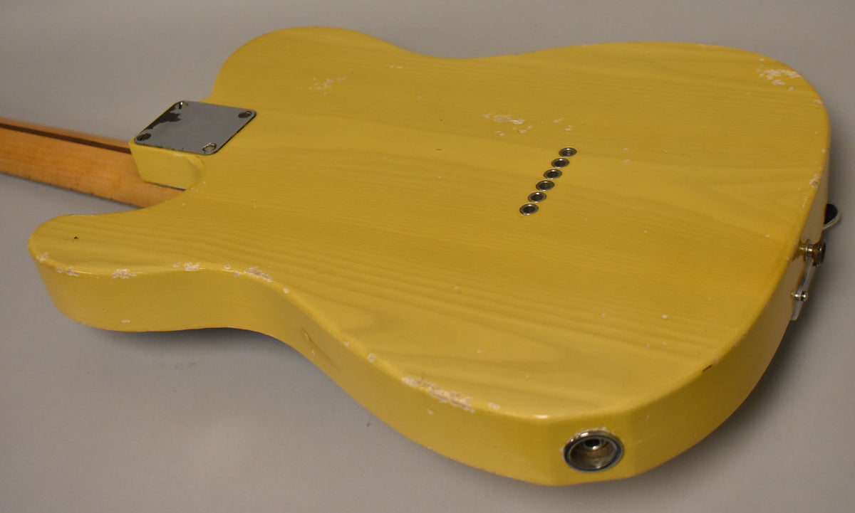 The back of a butterscotch blonde guitar body, showing wood grain, string ferrules, neck plate, and heavy finish wear.