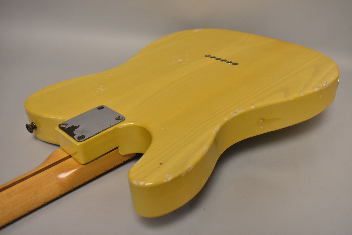 The butterscotch blonde guitar body, viewed from the back, shows significant wear, chips, and checking, with a worn chrome neck plate.