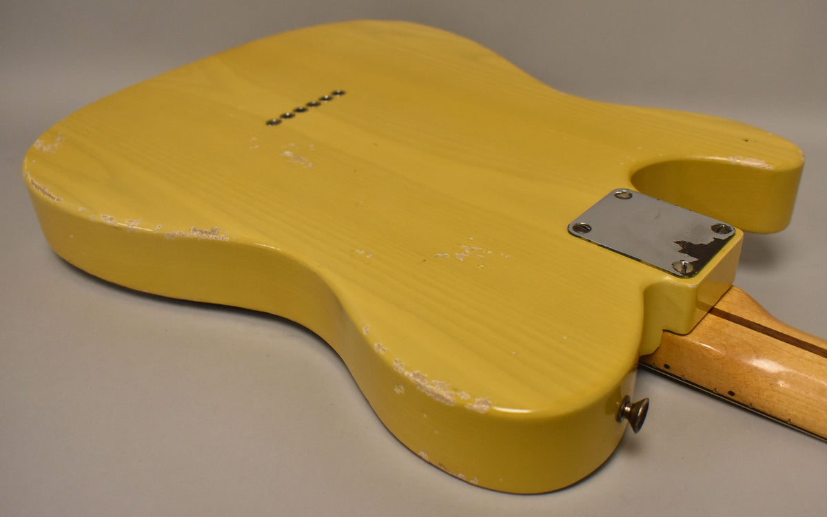 The back of a butterscotch blonde electric guitar shows heavy wear, checking, and chips in the finish, with a worn chrome neck plate.