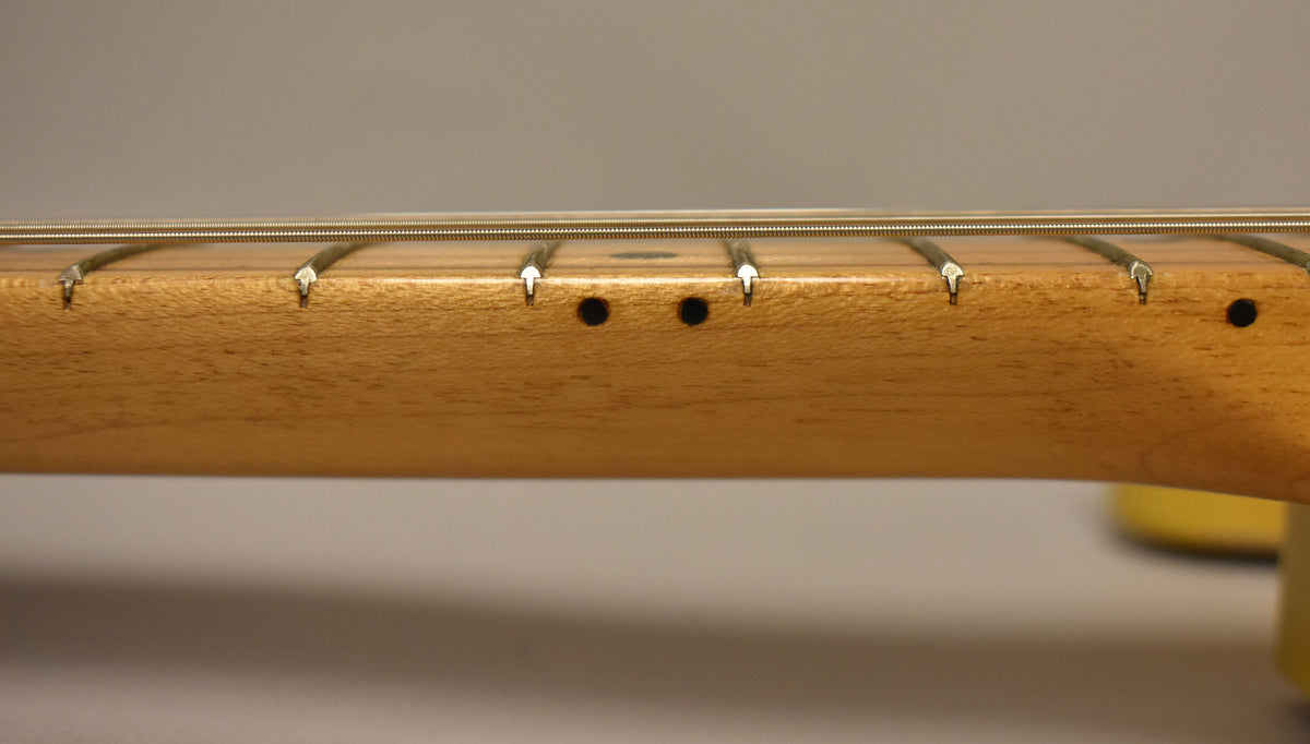 Close-up of the light blonde maple fretboard, showing three black dot inlays and light wear on the frets.
