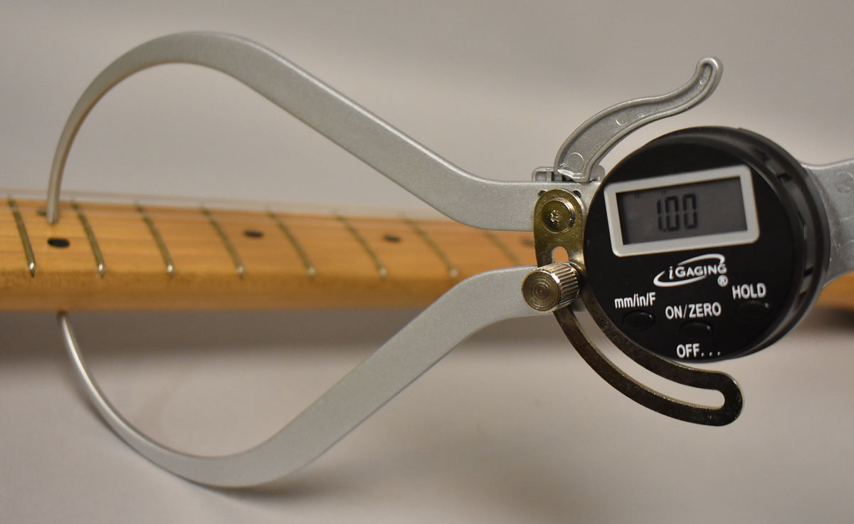A digital caliper measures the maple neck's thickness at the first fret, displaying "1.00" on its screen.