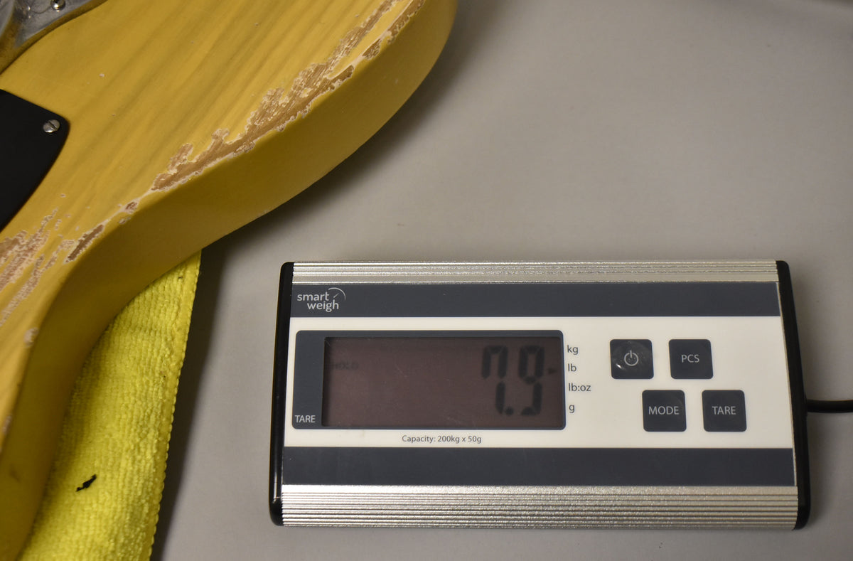 The guitar's butterscotch blonde body, showing significant wear and finish loss, rests on a scale displaying "7.9" pounds.