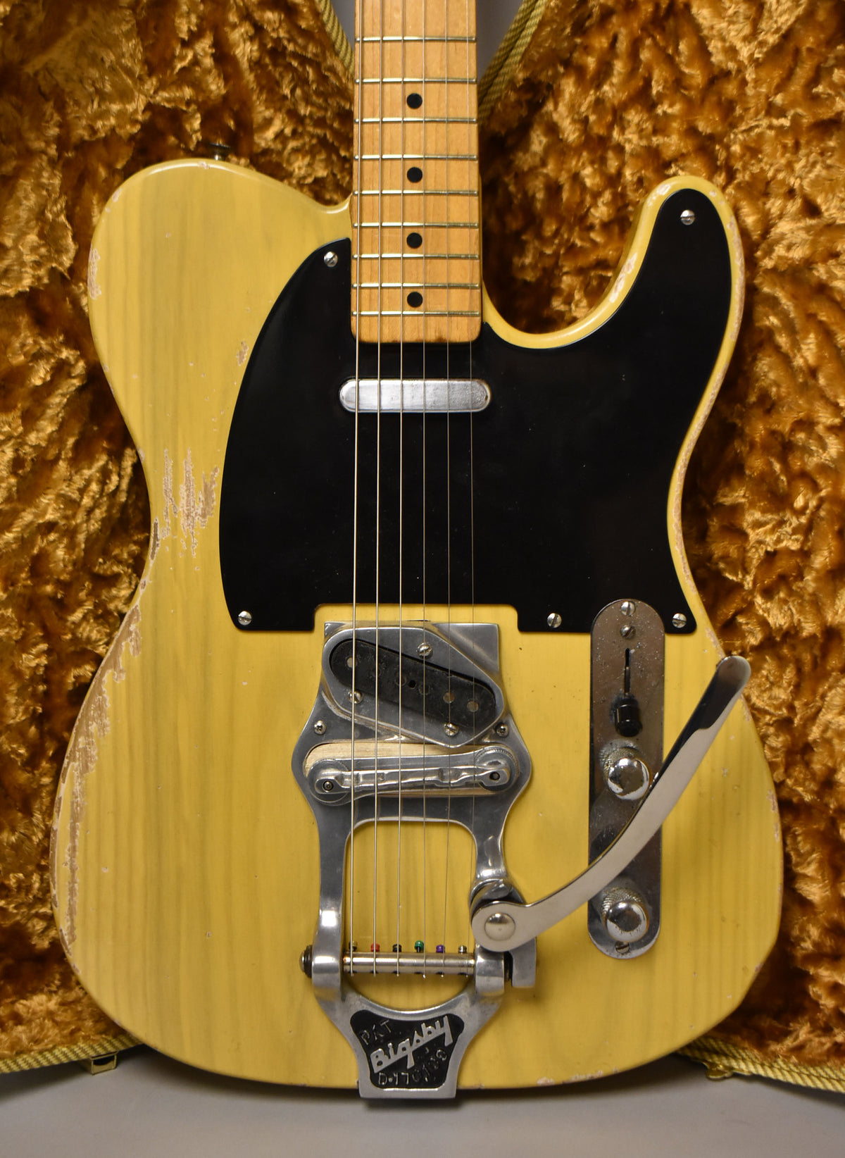 Full front view of a butterscotch blonde guitar with heavy wear, black pickguard, Bigsby tremolo, and a maple fretboard.