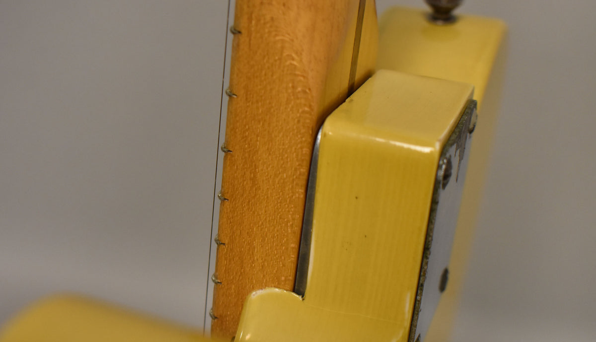 Close-up of the guitar's blonde body and neck joint, showing the neck plate with visible screws and some finish wear.