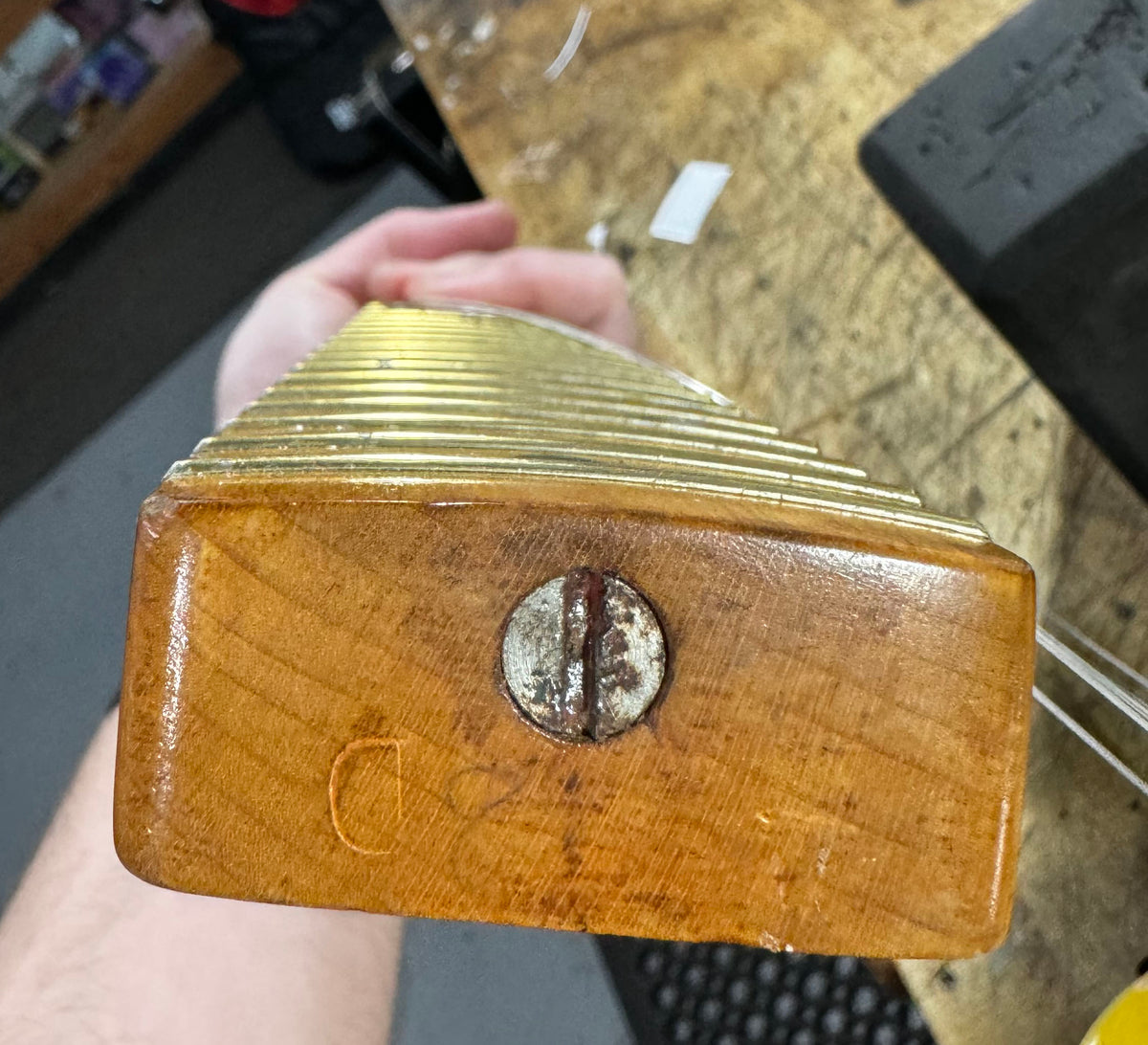 Close-up of the guitar neck heel, showing a worn, rusty screw and a faint stamped "D" on the ambered wood.