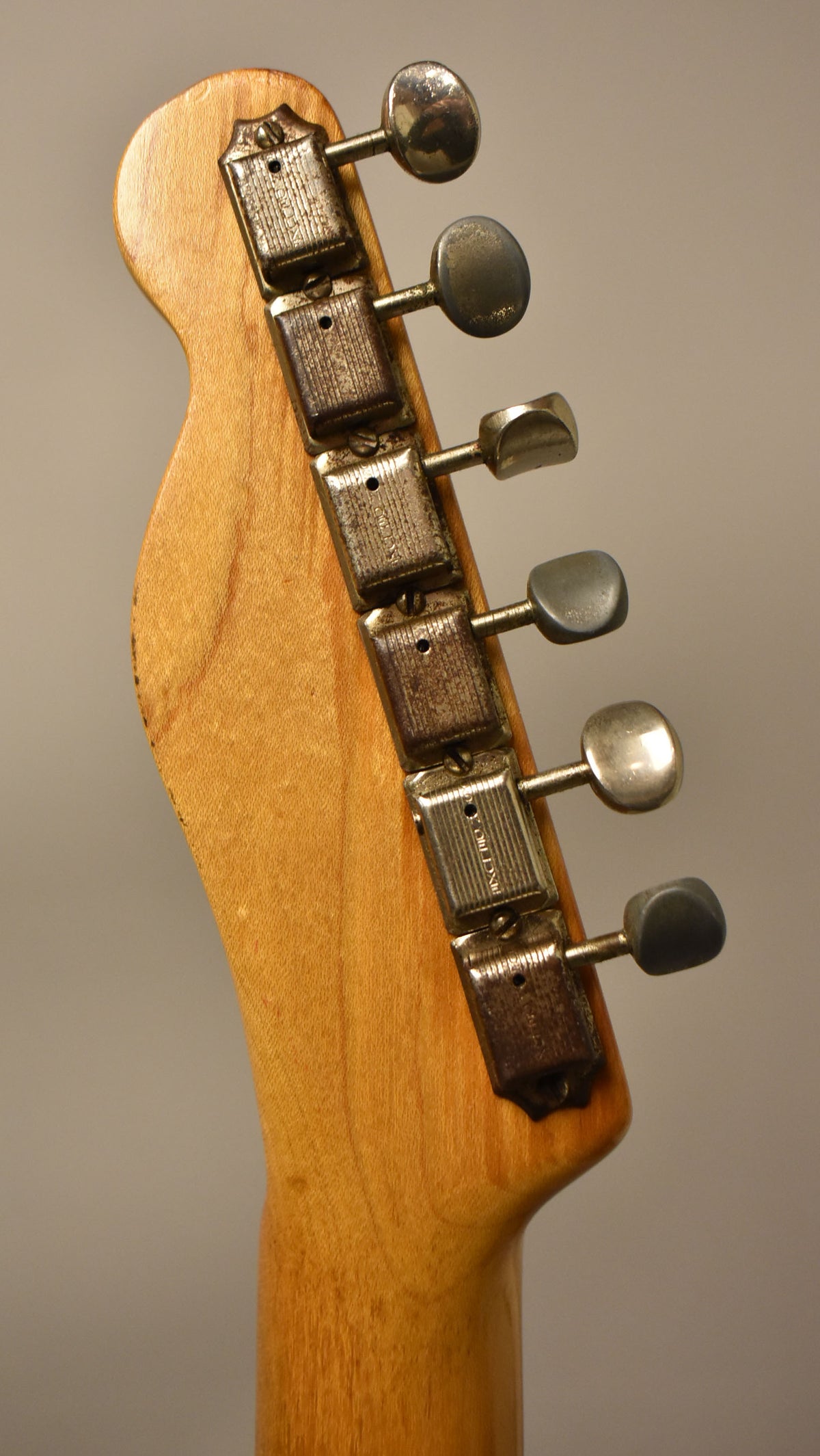 The back of the guitar's blonde headstock and neck, showing six heavily worn, tarnished metal tuners with oval buttons.