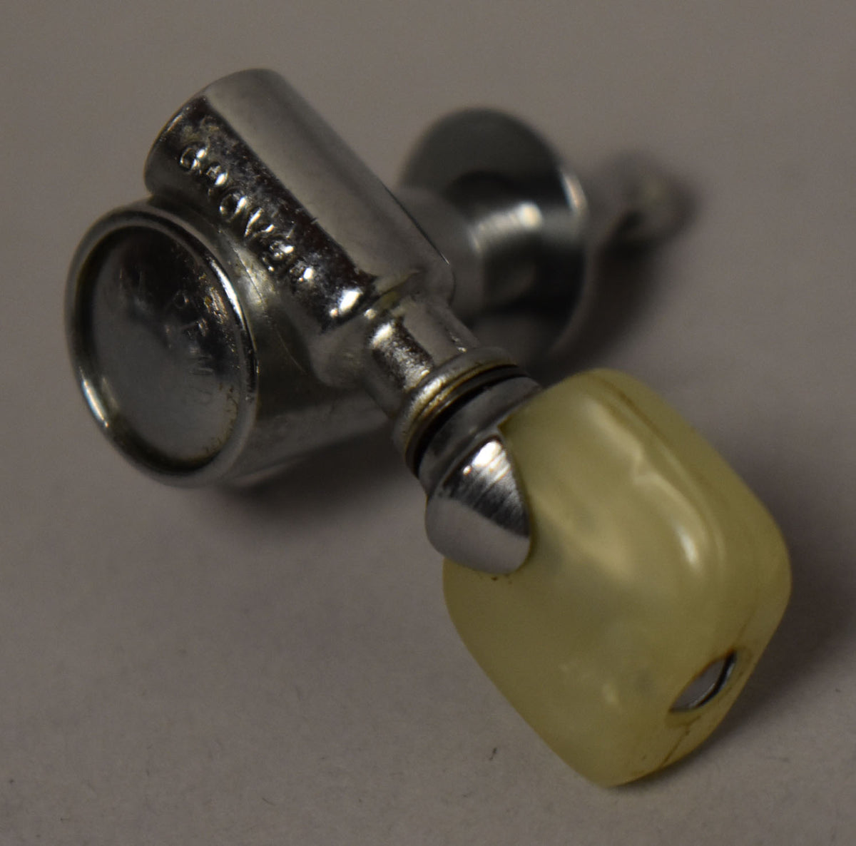 A single chrome tuner with a yellowed pearl button, viewed from above, showing some wear and grime.