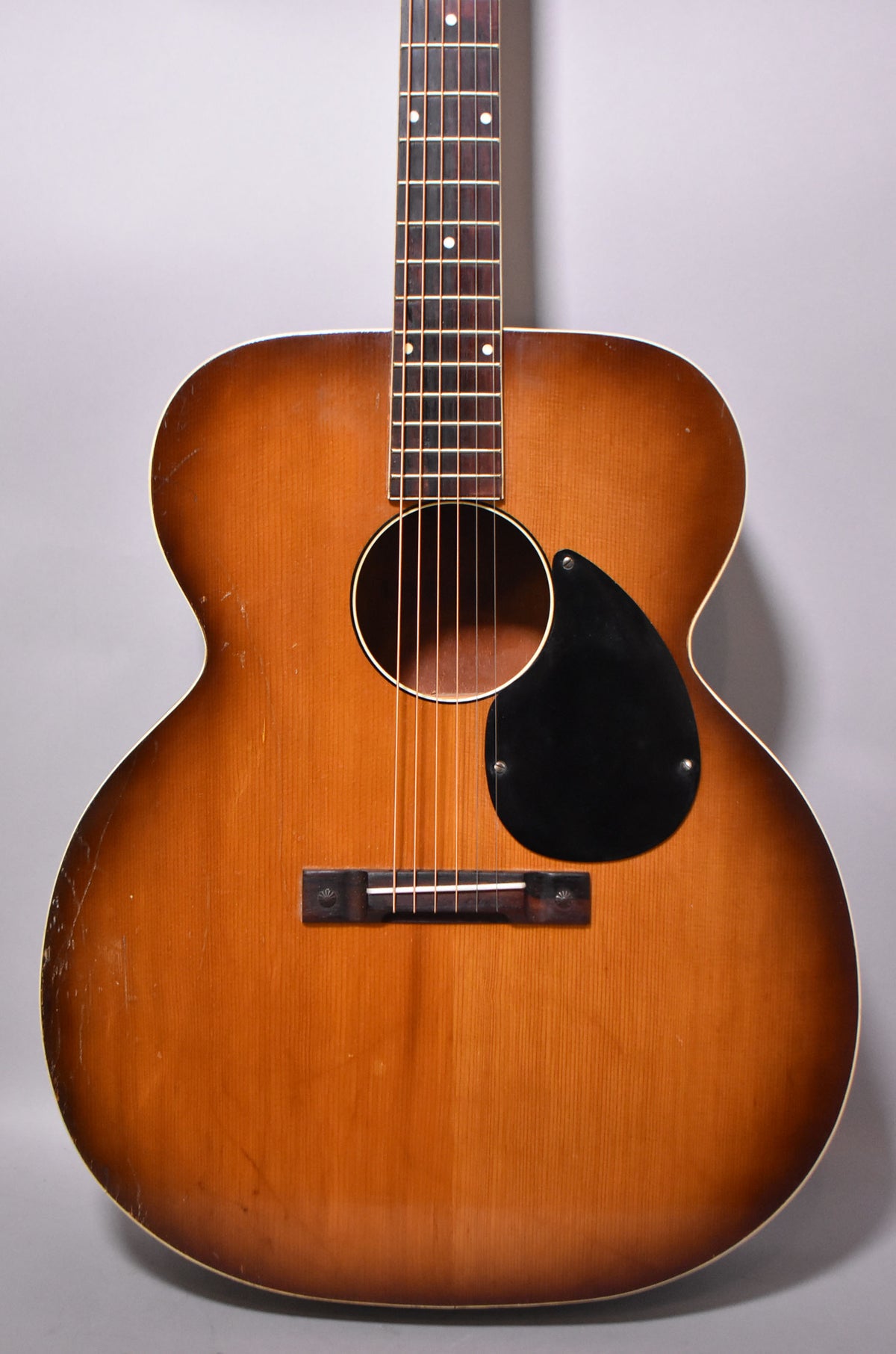 Full front view of a sunburst acoustic guitar with a black teardrop pickguard, showing visible finish wear and scratches.
