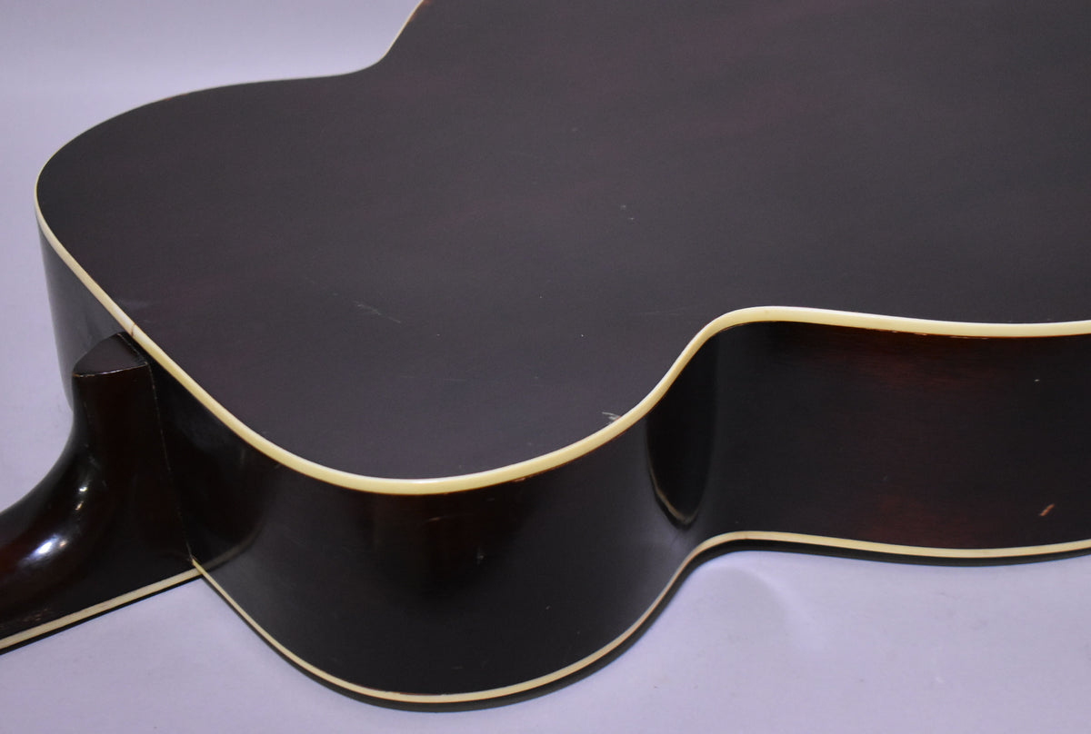 The dark sunburst acoustic guitar's lower bout and side are visible from the back, showing light wear and cream binding.