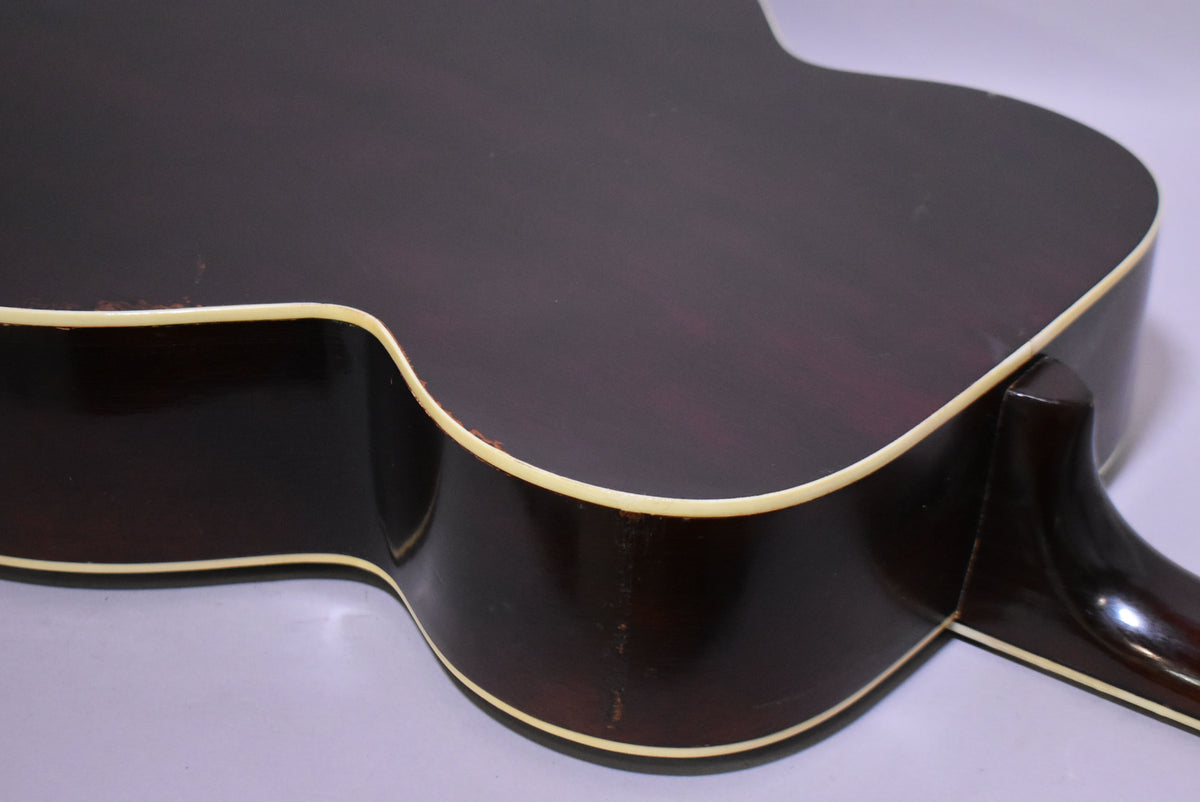 The lower bout of the dark sunburst acoustic guitar shows binding wear and finish checking along the body and neck heel.