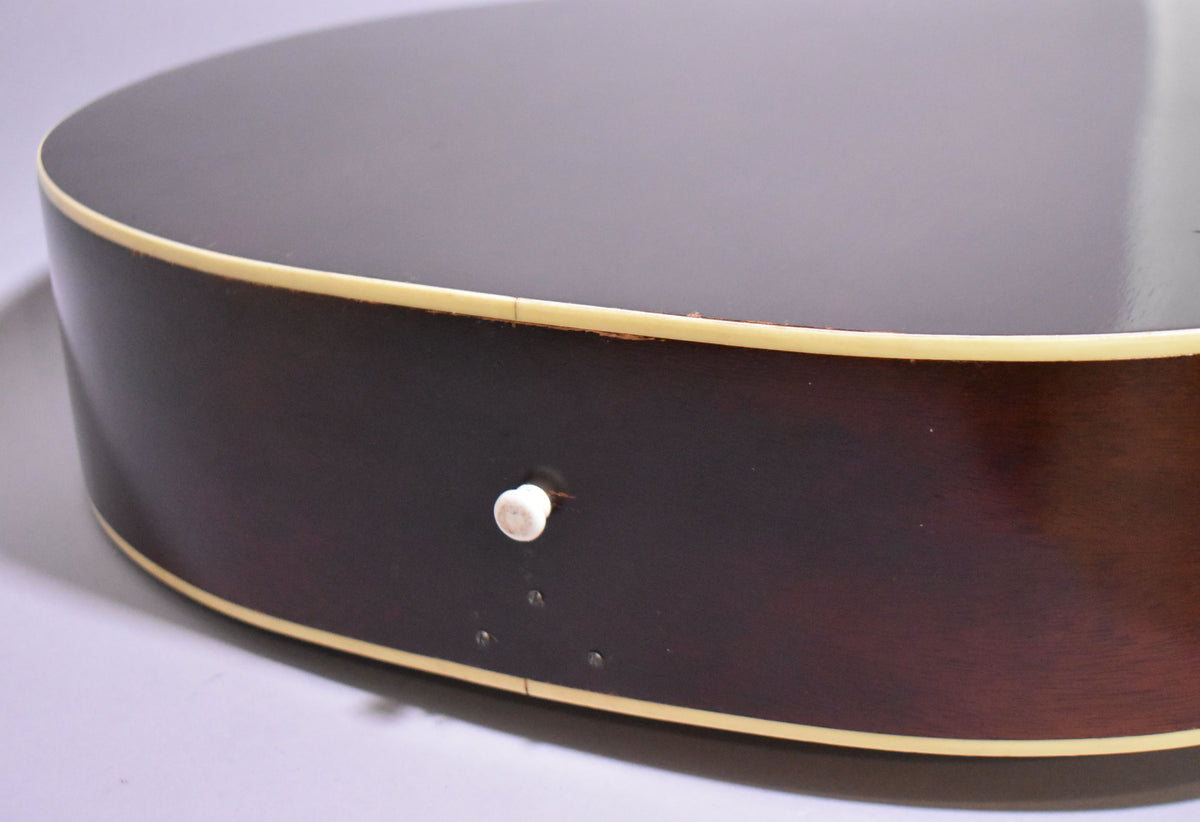Close-up of the guitar's lower bout, showing the dark sunburst finish, cream binding, and a white endpin jack with three small screws.